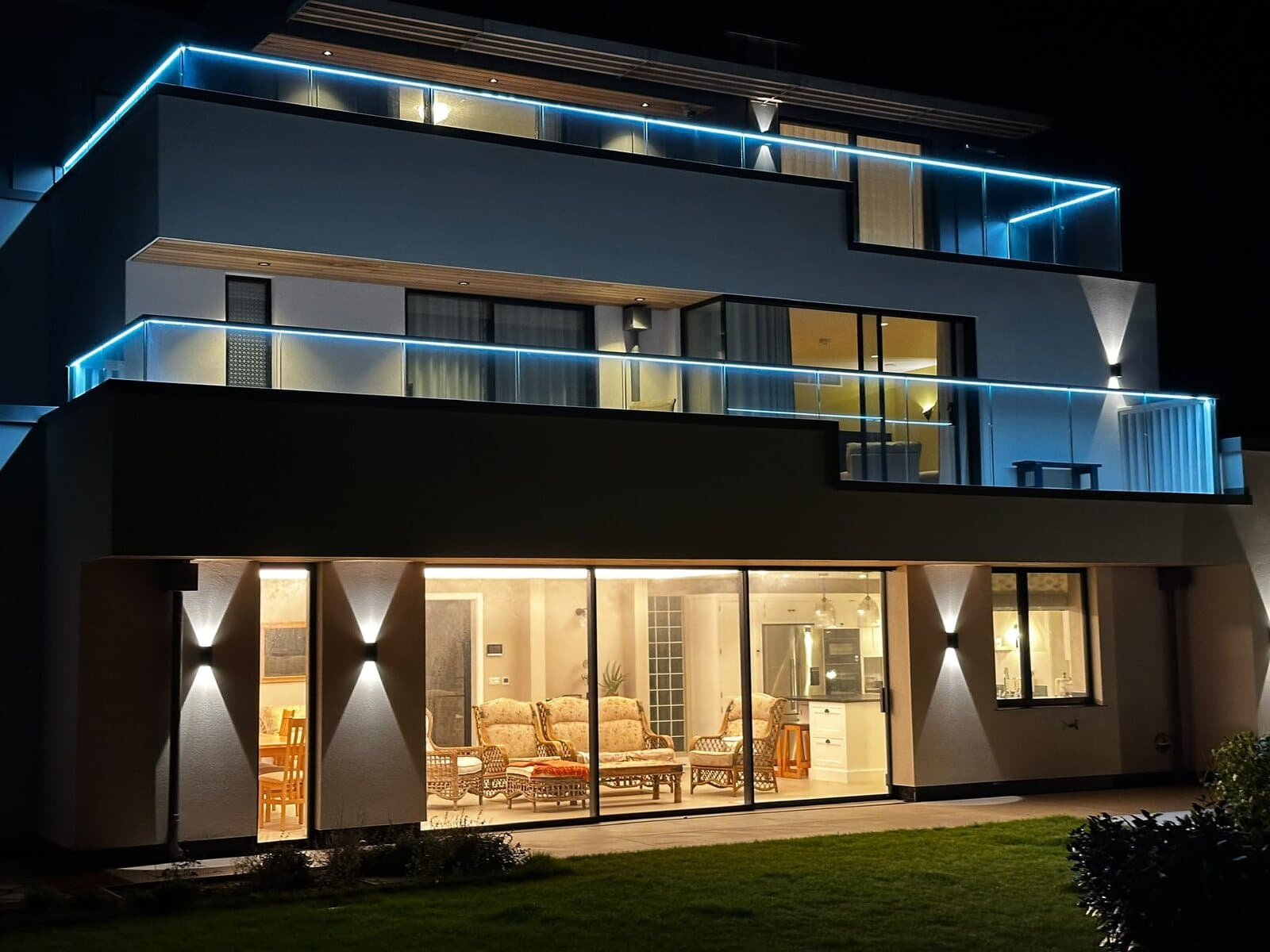 Back of a new build at night, with LED strips along both glass balconies and up and down wall lights by the sliding doors
