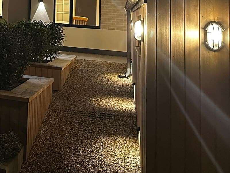 Gravel side path lit by low wall lights, with bulkhead lights on the timber cladding