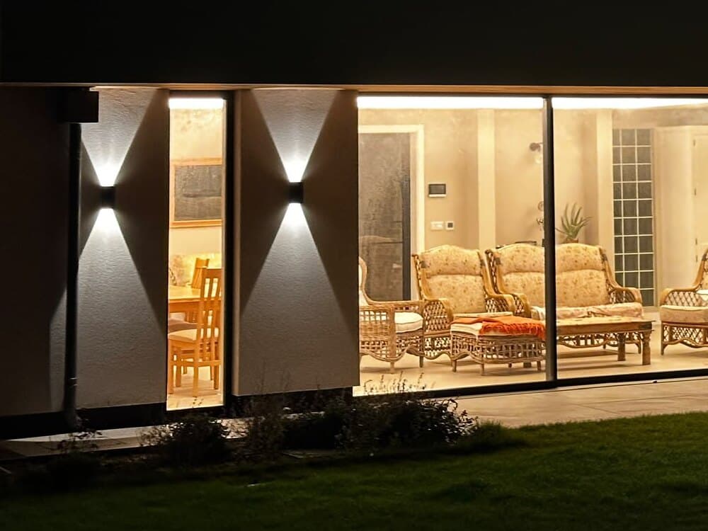 Up and down wall lights either side of a tall window, beside wide sliding glass doors onto the lawn